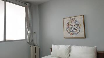 Een slaapkamer met een bed, een radiator, een raam met gordijnen en een aan de muur bevestigd fotolijstje.