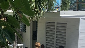 Ein kleiner Sitzbereich im Freien mit weißer Brüstung, umgeben von Grünpflanzen und einem Gebäude mit Fensterläden, ebenfalls in Weiß.