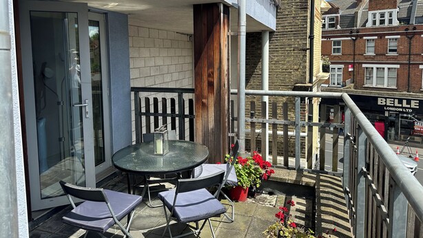A balcony with a glass door, a round table with chairs, and potted plants.