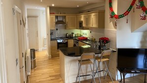 A modern kitchen with wooden cabinets, a central island with bar stools, a built-in stove, and a large flat-screen TV.