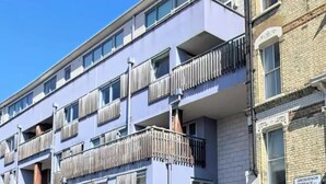 A multi-story building with balconies, a closed shop on the ground floor, and a clear blue sky.