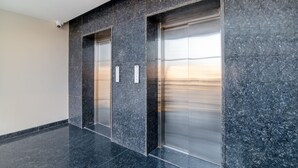 A modern elevator with a metallic finish, set in a hallway with dark granite walls and a polished floor.