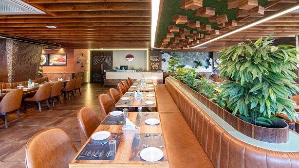 A restaurant with wooden ceiling beams, a long counter with a plant, and booths with menus.