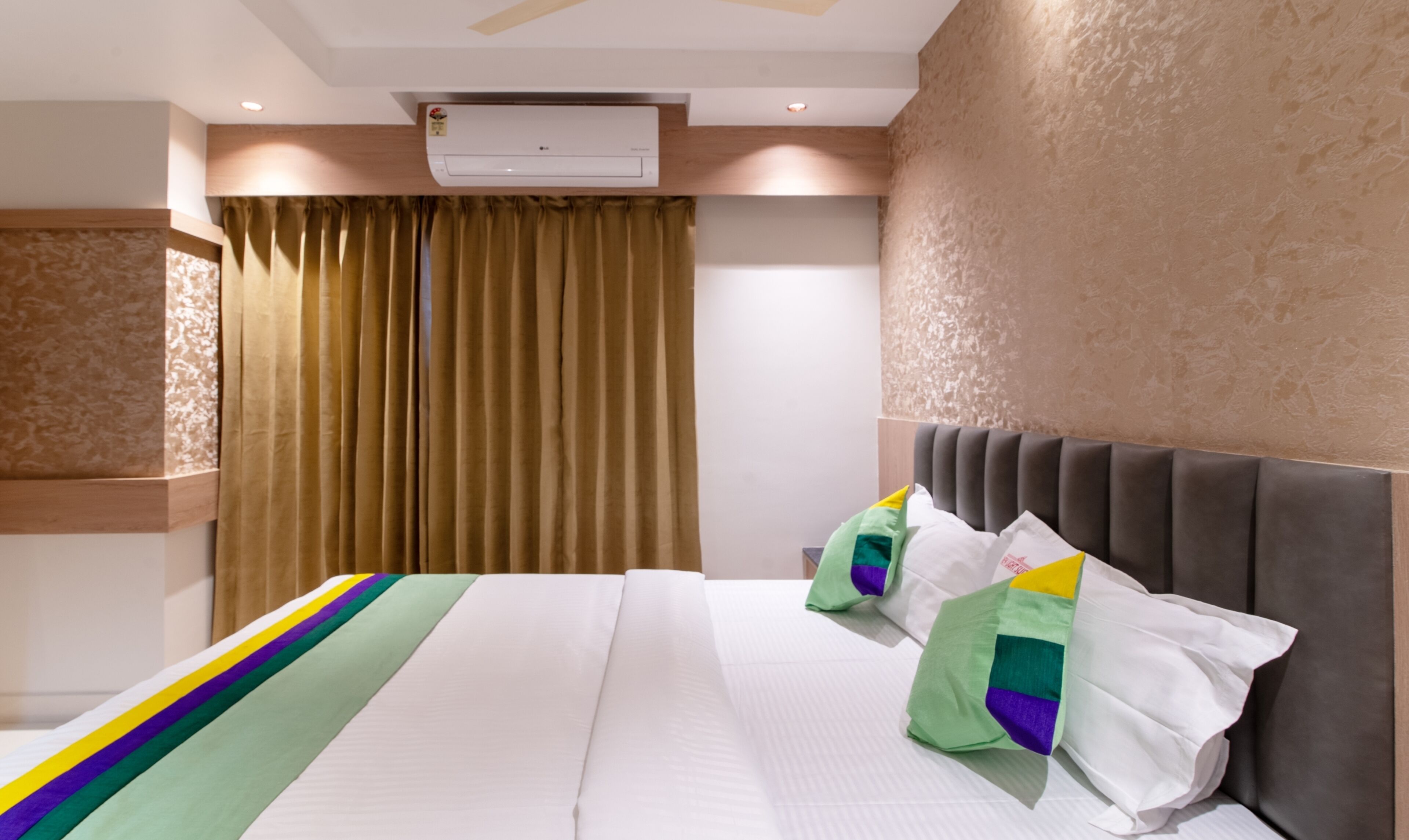 A hotel room with a bed, curtains, an air conditioning unit, and a textured wall.