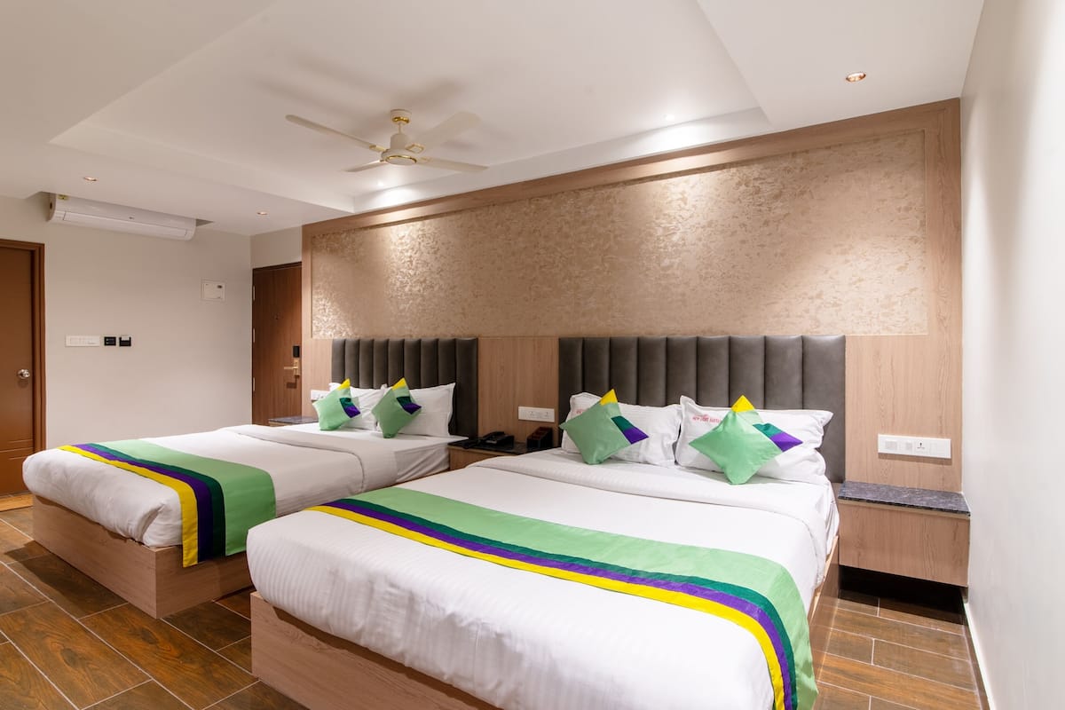 Habitación de hotel con dos camas, un ventilador de techo, pared con textura y puerta de madera.
