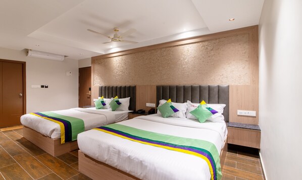 A hotel room with two beds, a ceiling fan, a textured wall, and a wooden door. - Treebo Premium New Light Suites (Bengaluru)