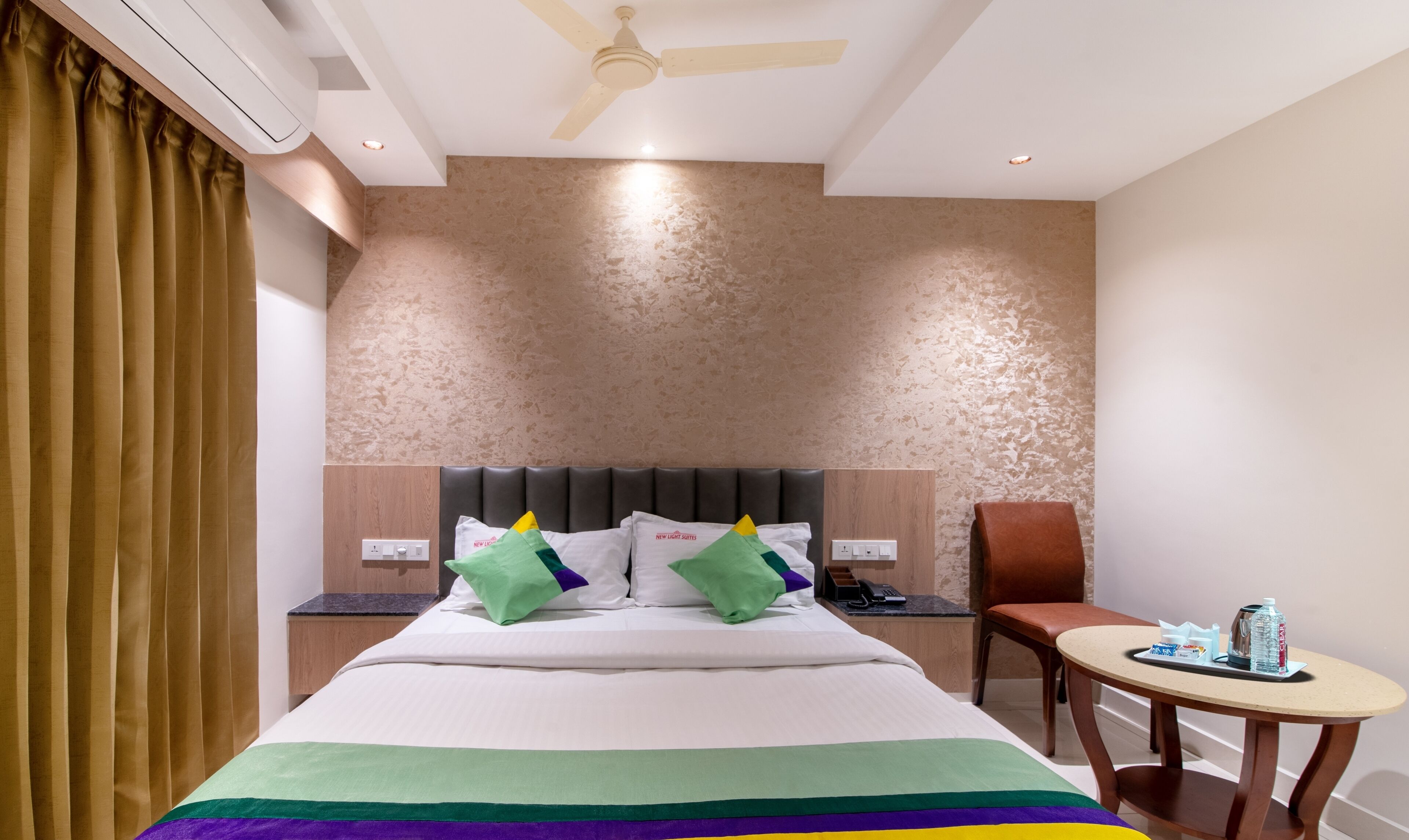 A hotel room with a bed, a chair, a small table, a ceiling fan, and a wall with a textured pattern.
