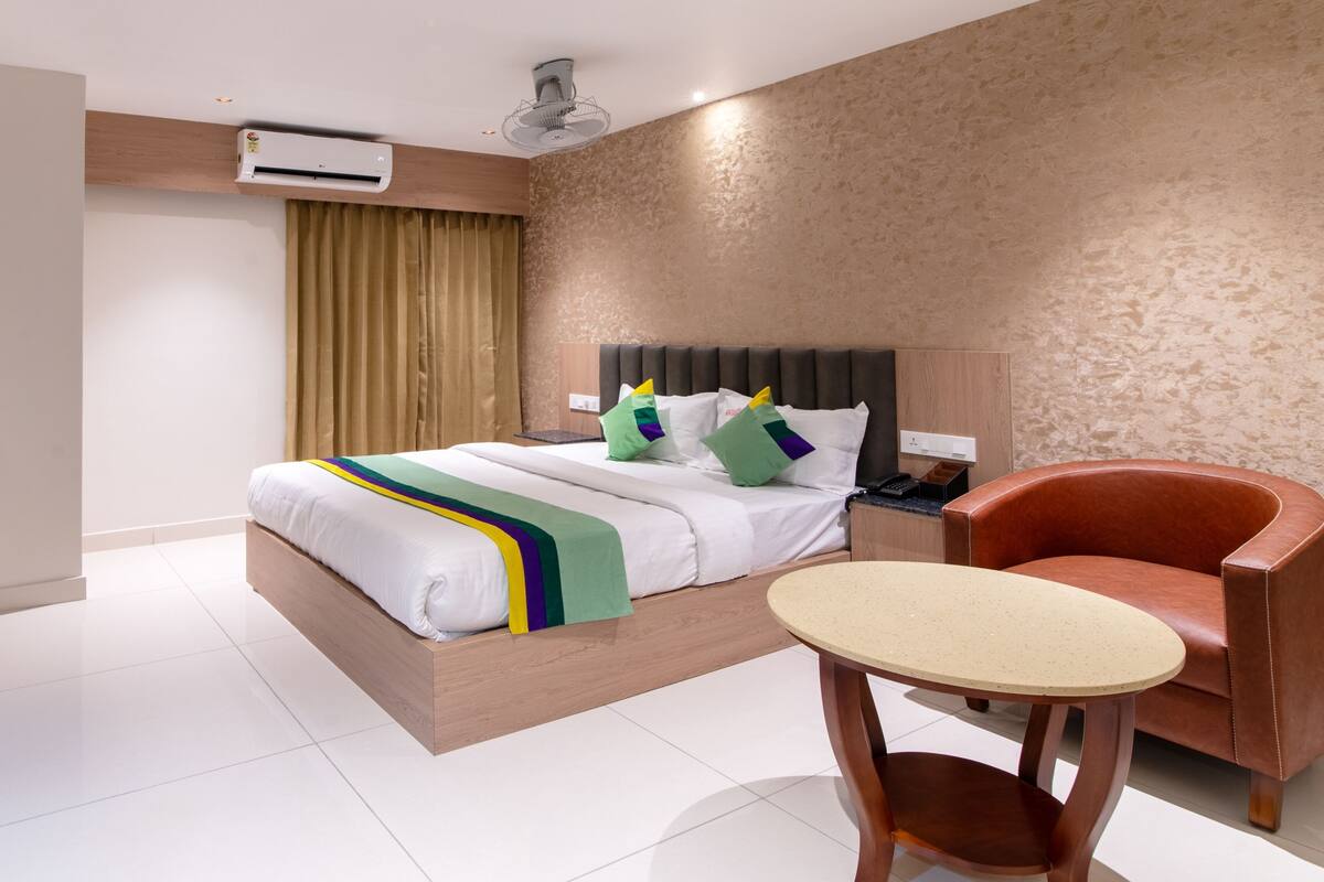 Habitación de hotel con cama, una silla, una mesa, un equipo de aire acondicionado y un ventilador de pared.