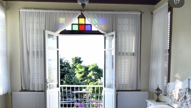 Una camera da letto con un letto grande, vista sull'esterno attraverso una finestra aperta e un balcone con ringhiera.