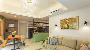 A modern living room with a sofa, a coffee table, and a dining area with a table and chairs. There is a kitchen area with a green island and a sink.