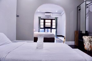 Habitación de hotel con una cama grande, una mesita pequeña y vista a otra habitación por un arco.