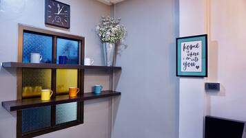 Quarto com relógio fixado na parede, quadro com frase motivacional e prateleiras com objetos decorativos e canecas.