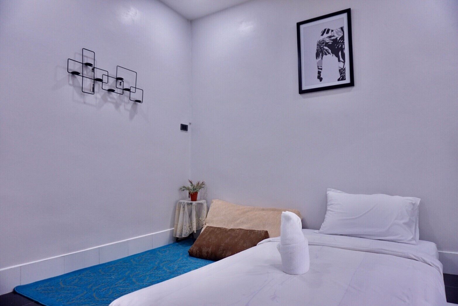 Habitación de hotel con cama, una mesita con una planta, una obra de arte en la pared y una lámpara con forma geométrica.
