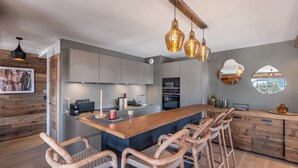 A modern kitchen with a central island, bar stools, and pendant lighting.