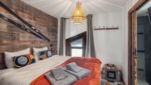 A bedroom with a wooden headboard, a large bed with multiple pillows, a hanging light fixture, and a view of the outdoors through a door.