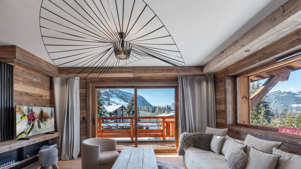 A modern living room with a wooden ceiling, a large TV, a wooden coffee table, and a sofa with a view of a snowy mountain.