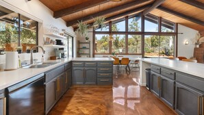 Una cocina amplia con una isla grande, vigas de madera en el techo y grandes ventanas con vistas al exterior.