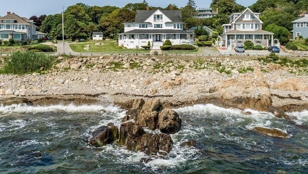 Uma propriedade costeira com várias casas, uma linha costeira rochosa e vista clara para o oceano.