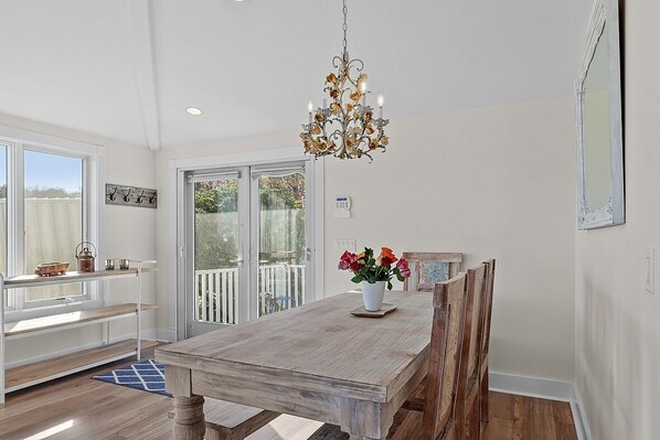Un espace repas avec une table en bois, un lustre et une vue à travers des portes vitrées.