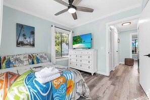 A bedroom with a bed, a dresser, a ceiling fan, a TV, and a window with blinds.