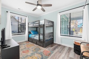 A room with a bunk bed, a desk, a television, and a ceiling fan.