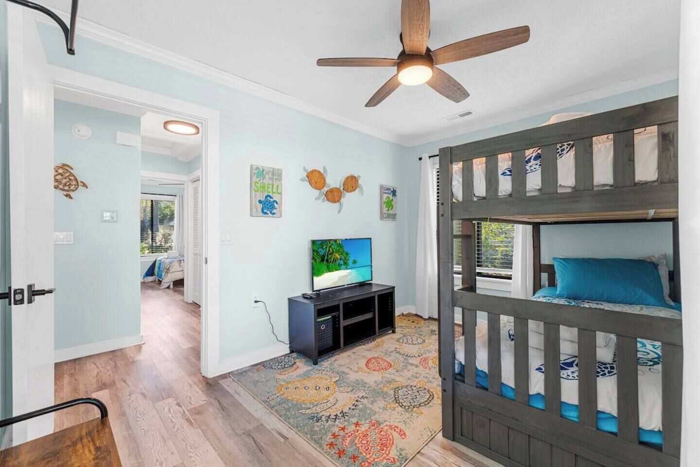 Une chambre avec un lit superposé, une télévision, un ventilateur de plafond et un tapis à motifs.