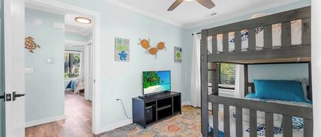 A room with a bunk bed, a television, a ceiling fan, and a patterned rug.