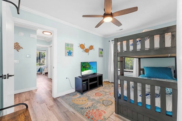 Une chambre avec un lit superposé, une télévision, un ventilateur de plafond et un tapis à motifs.