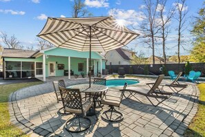 A backyard with a swimming pool, patio furniture, and a covered seating area.