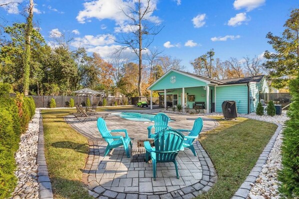 A backyard with a swimming pool, outdoor seating, and a covered patio area.