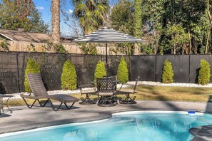 A swimming pool with lounge chairs and a table, surrounded by a fence and trees.