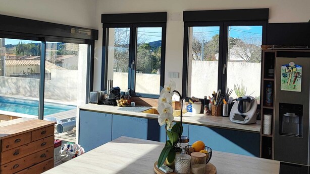 A modern kitchen with large windows, a wooden island, and a view of a swimming pool.