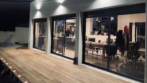 An outdoor patio area with a wooden deck, large glass windows, and a modern building facade.