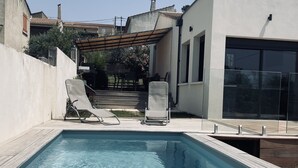 A swimming pool with clear water, surrounded by a concrete deck and two lounge chairs.