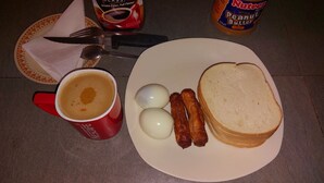 Un plato con huevos, salchichas y tostadas, una taza roja con café, y un tarro de Nutella.