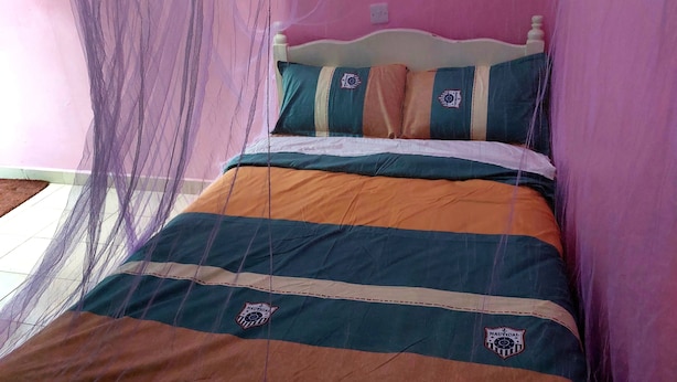 Una cama con colcha azul marino y anaranjada a rayas, dos almohadas con un emblema náutico y un dosel con mosquitero púrpura.
