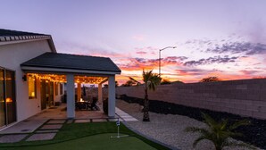 Ein modernes Haus mit überdachter Terrasse, gepflegtem Rasen und Blick auf den Sonnenuntergang.