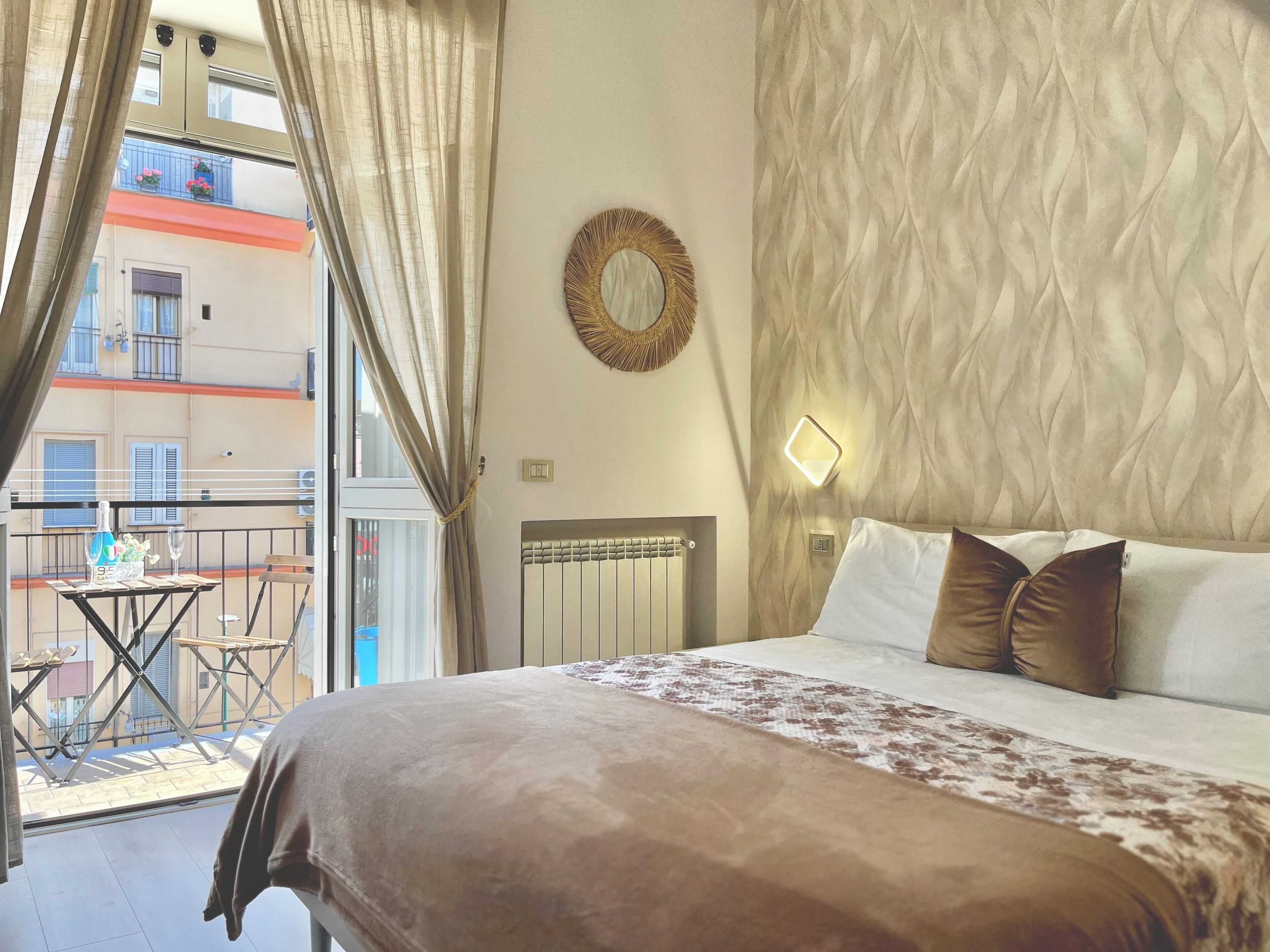 Ett hotellrum med en stor säng, utsikt över balkongen, en rund spegel på väggen och ett element.