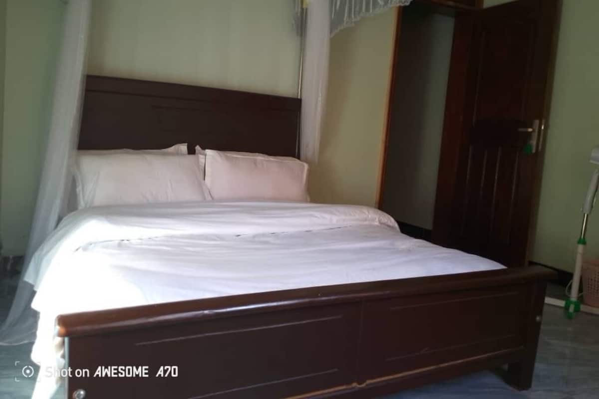 A single bed with a wooden frame and white bedding in a room with a wooden door and a curtain.