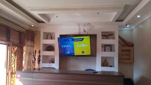 A reception area with a large flat-screen TV mounted on the wall, a wooden reception desk, and a decorative shelf with items.