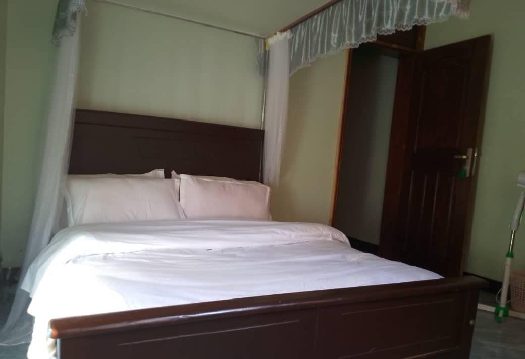 Uma cama de solteiro com estrutura de madeira e roupa de cama branca em um quarto com porta de madeira e cortina.