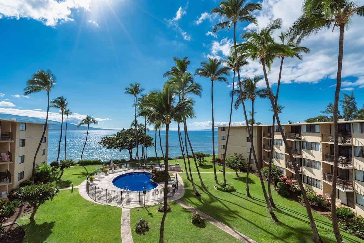 A hotel with a pool surrounded by palm trees and a view of the ocean.