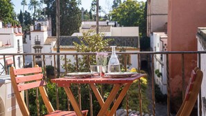 A wooden table set with a glass, a bottle, and a vase with flowers, on a balcony with a view of buildings and trees. - Historic House in the City Center (Sevilla)