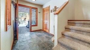 Un couloir avec une porte en bois, un escalier et un sol carrelé en pierre.