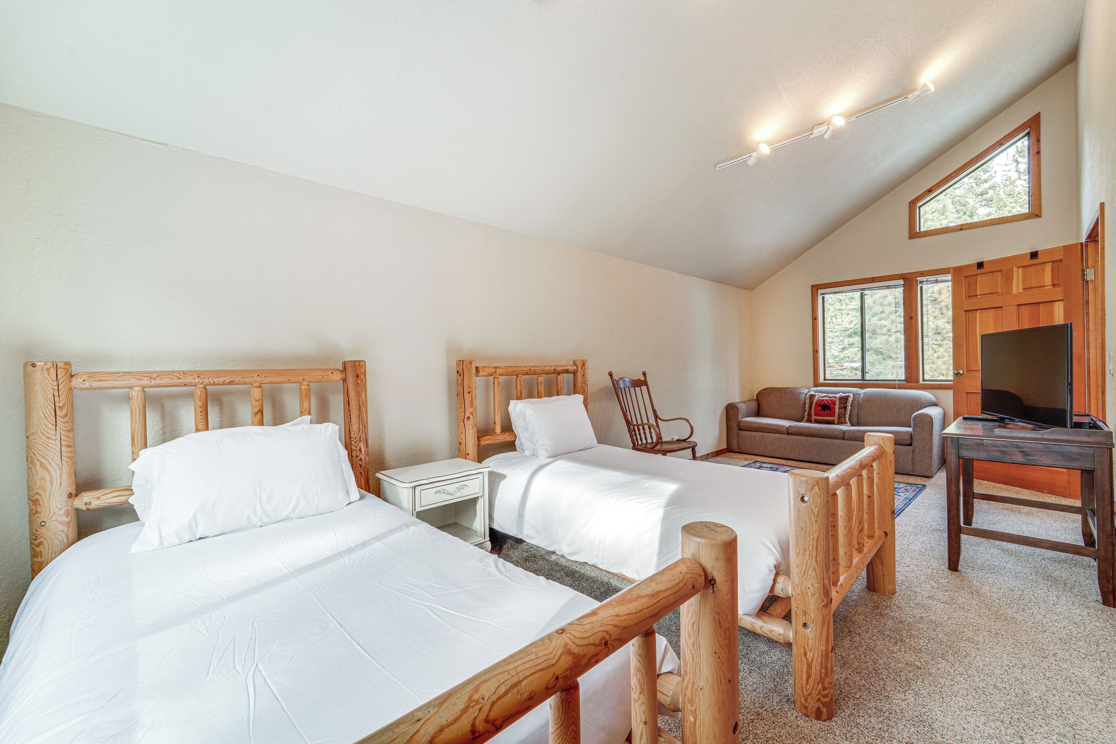 A bedroom with two wooden beds, a sofa, a TV, and a desk.