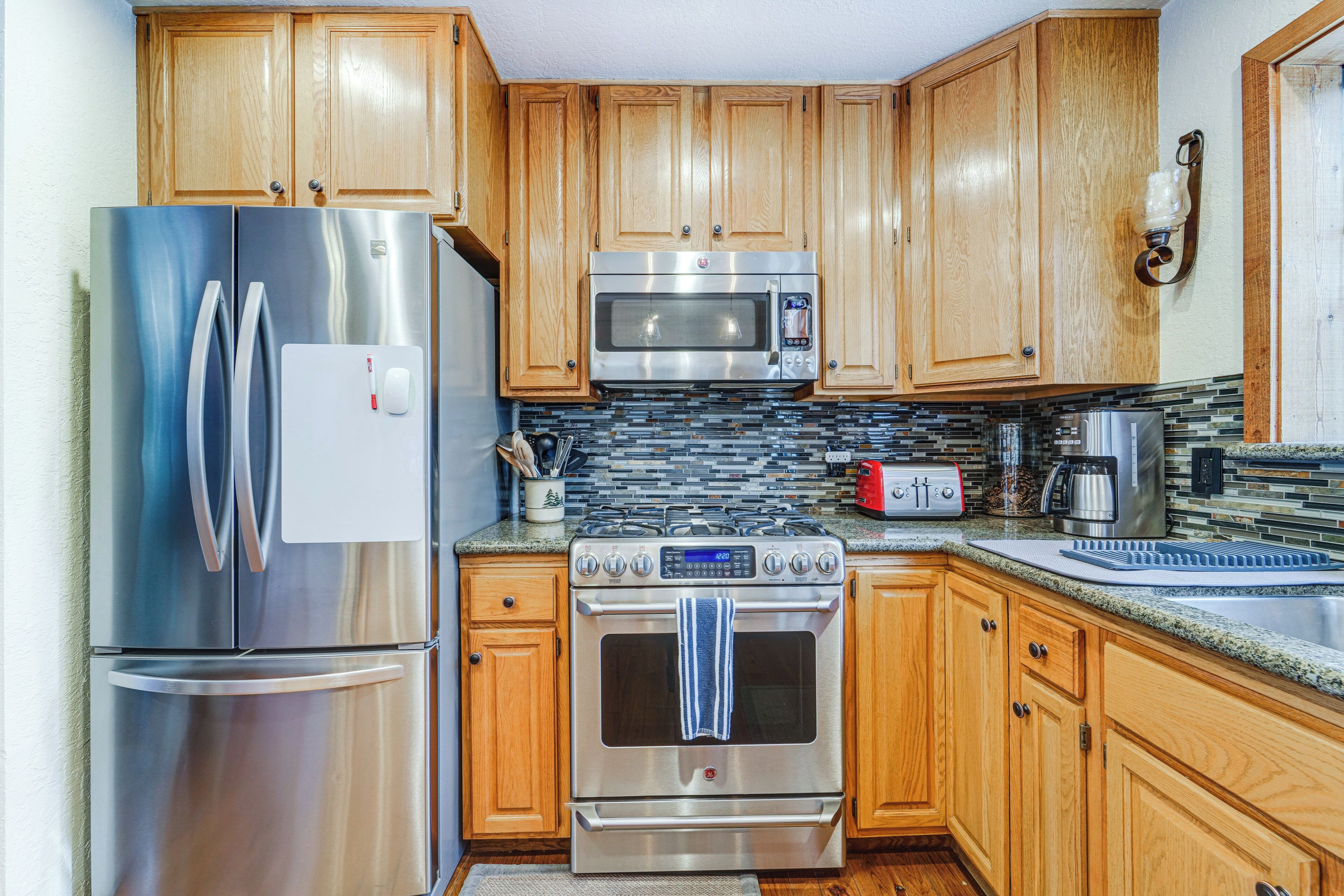 A kitchen with wooden cabinets, stainless steel appliances, a tiled backsplash, and a granite countertop.