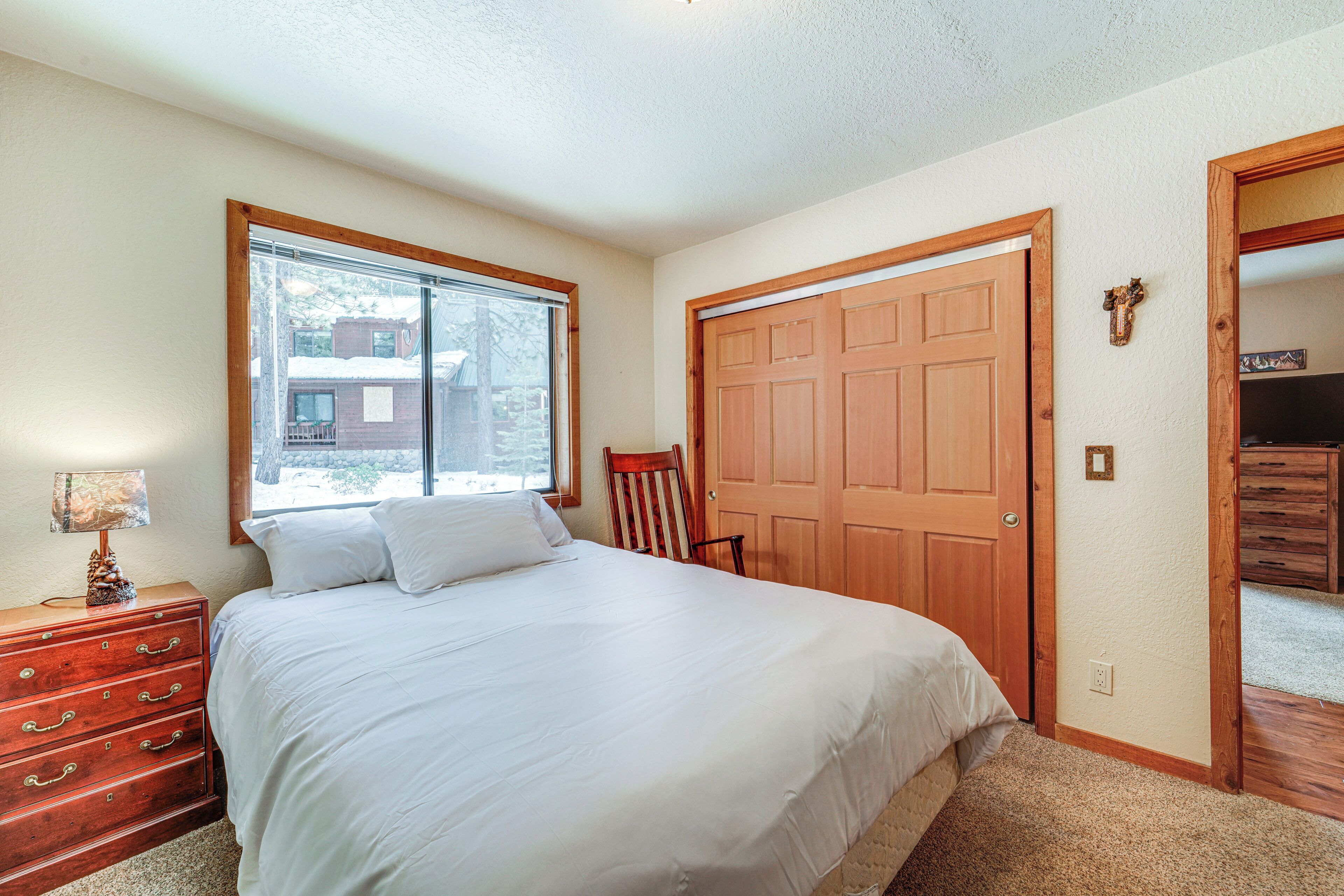 A bedroom with a large bed, wooden dresser, and a window with a view of a house.