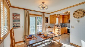 A dining area with a wooden table set for four, a kitchen in the background, and a large wall clock. - Spacious Ouray Townhome - Walk to Hot Springs! (Ouray)