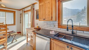 A kitchen with wooden cabinets, a black countertop, a built-in dishwasher, and a window with a view of mountains. - Spacious Ouray Townhome - Walk to Hot Springs! (Ouray)