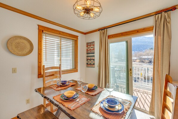 Un comedor con mesa de madera dispuesta para cuatro, un tapiz de fibras y vistas a un paisaje montañoso a través de puertas correderas de vidrio.